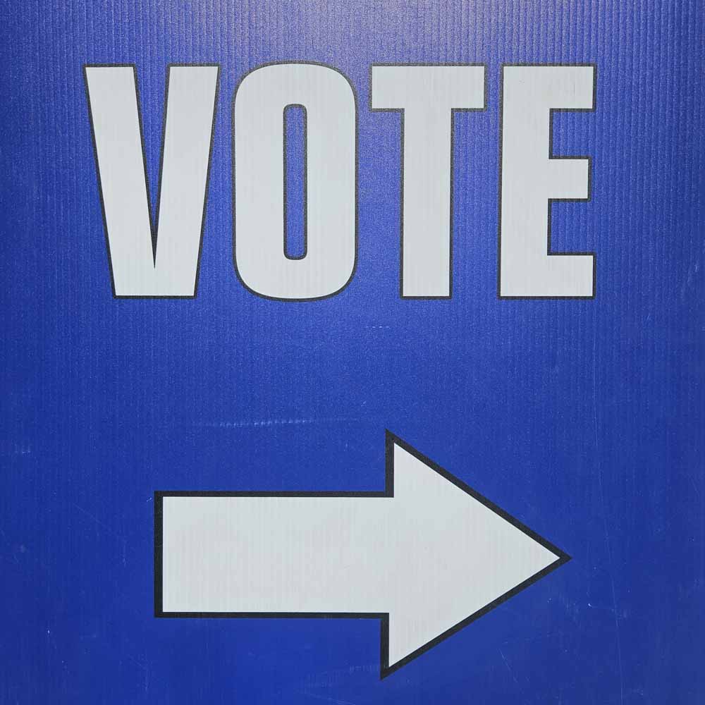 VOTE with an arrow in white letters on a blue background.